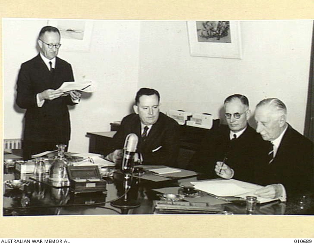 The Governor General, Lord Gowrie, reading the proclamation announcing that Australia is at war with Japan.  From left, the Secretary Prime Minister's Department, Mr F Strahan; Minister for the Army, Mr Forde; Prime MInister Mr Curtain; and Lord Gowrie. 