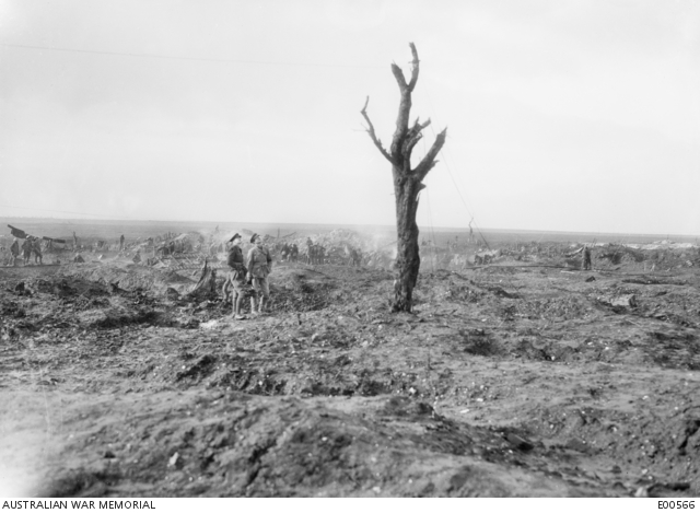 Black and white photo of two soldiers looking at lone tree at Mouquet Farm amid the battlefield destruction.